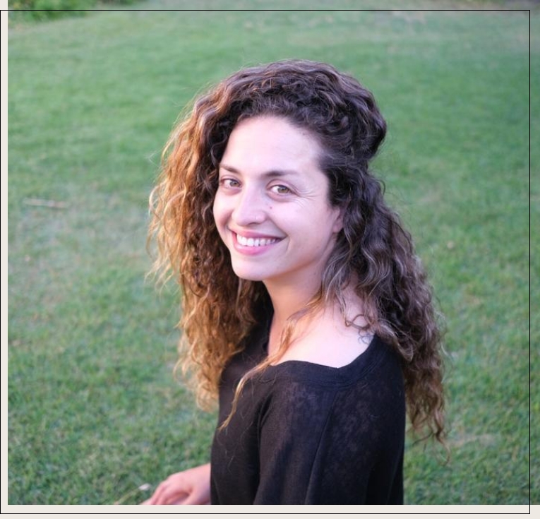 תמונה של אישה מחייכת אשר לובשת חולצה שחורה ויושבת על דשא