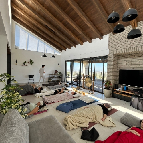 קבוצה של נשים אשר שוכבות על מזרנים באמצע סדנא של הילניג ונרגעות ועל הפנים יש להן מגבת ועל הגוף שמיכה