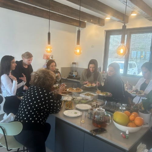 קבוצה של נשים עומדות מסביב לשולחן מדברות ואוכלות מהאוכל על השולחן